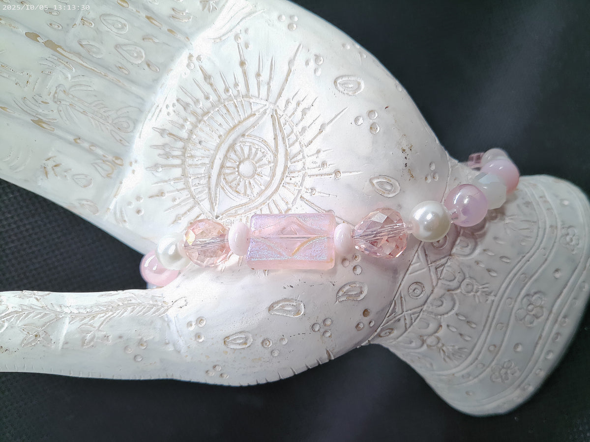 A pink beaded bracelet with a central faceted pink crystal and white pearl-like beads, displayed on a white carved hand-shaped stand against a dark background.